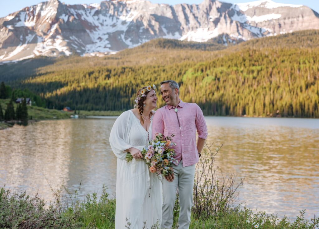 Bride and groom holding hands and looking at each other surrounded by mountains and lake scenery in Telluride