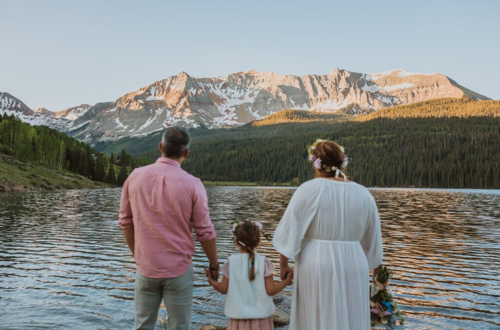 Bride and groom holding daughter's hand looking away from camera at scenery in Telluride