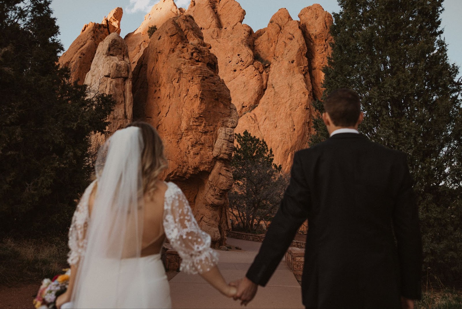 Bride and groom holding hands facing large red rock at Garden of the Gods