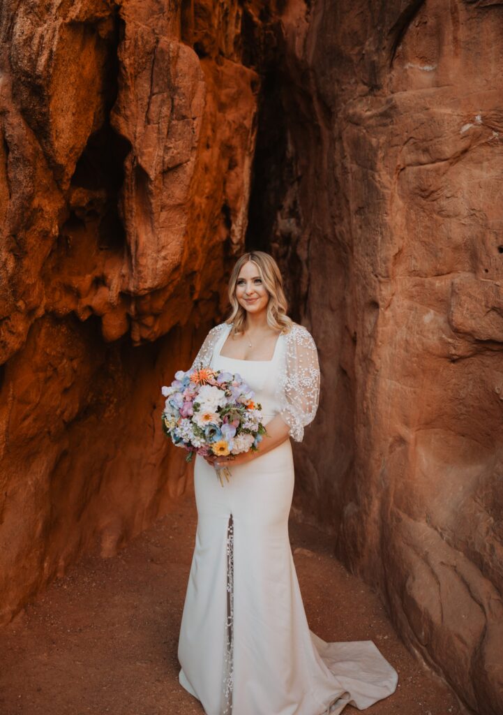 Bride smiling at camera and holding flowers surrounded by a red rock formation at Garden of the Gods