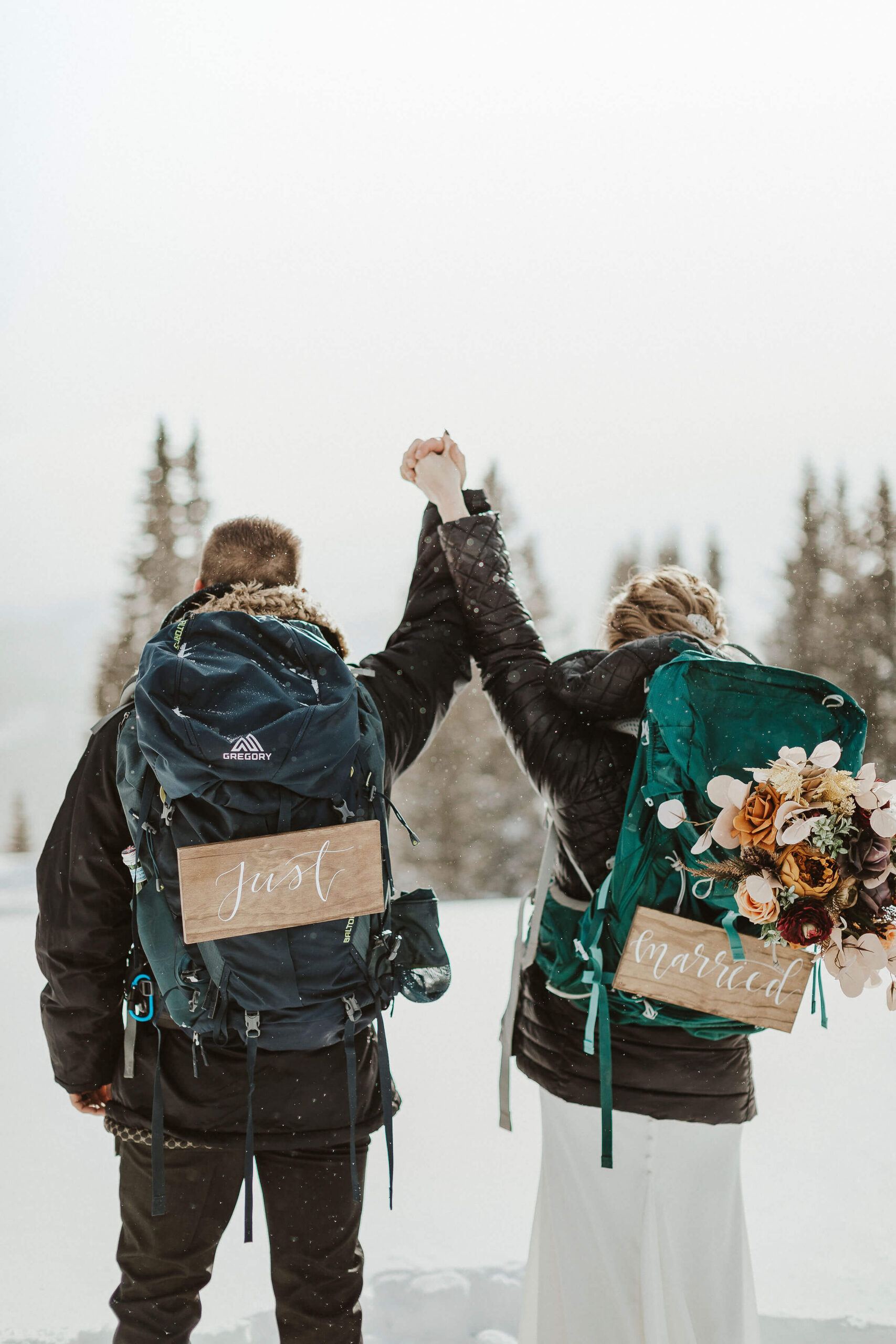elopement couple standing in the snow with backpacks showing signs that say just married to represent elopement ideas