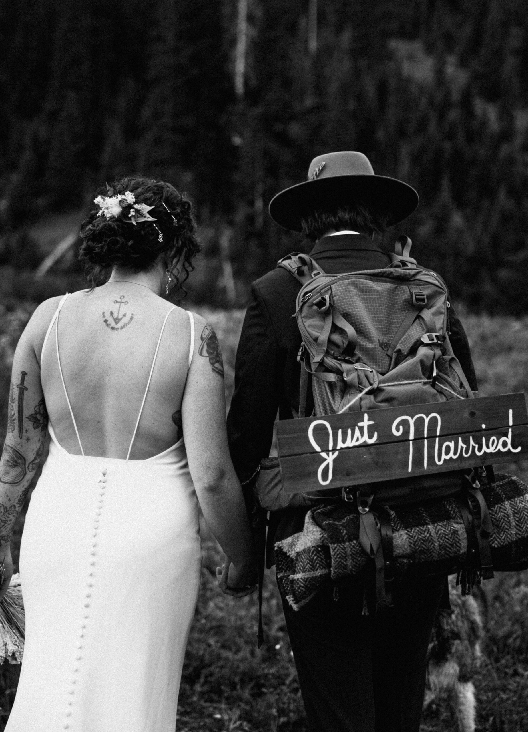 elopement couple posing with backs to camera and backpack with just married sign