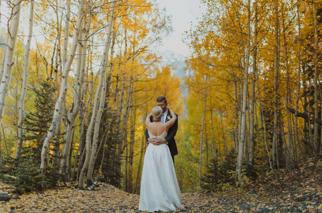 bride and groom hugging surrounded by trees and fall foliage for Ouray elopement