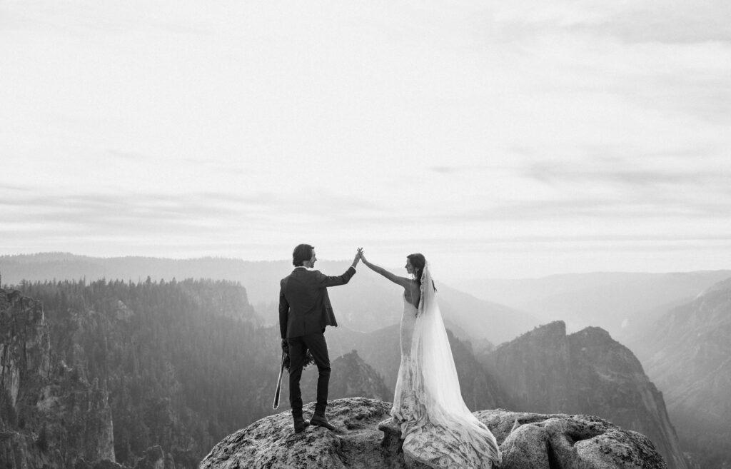 elopement couple holding hands in air surrounded by Yosemite National Park mountain views
