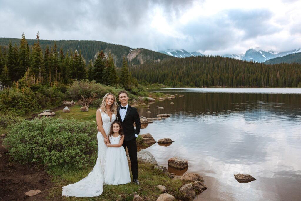 Bride and groom posing with daughter at wedding next to lake in Colorado