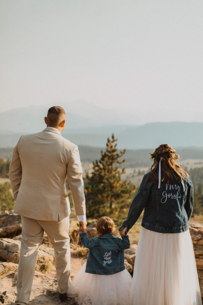 bride, groom, and child with backs facing camera posing for Rocky Mountain National Park wedding photos