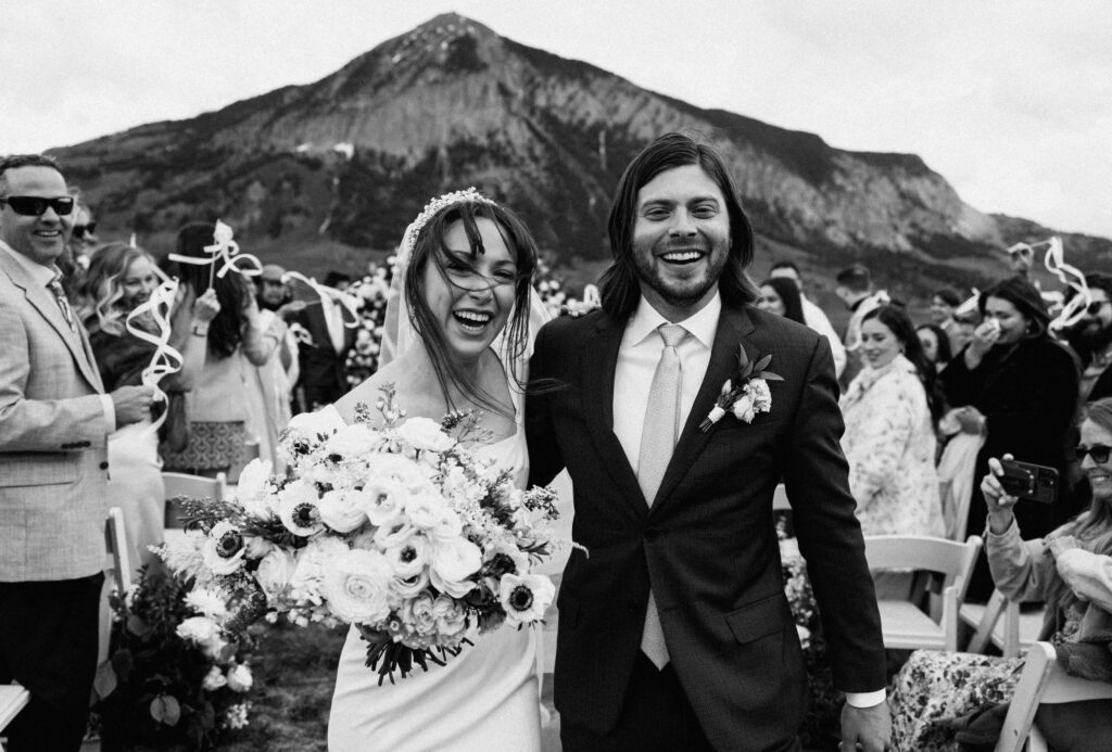 bride and groom smiling at wedding in Colorado with guests behind them
