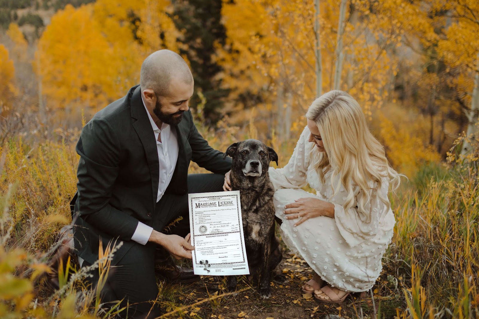 bride and groom posing with their dog and holding marriage license