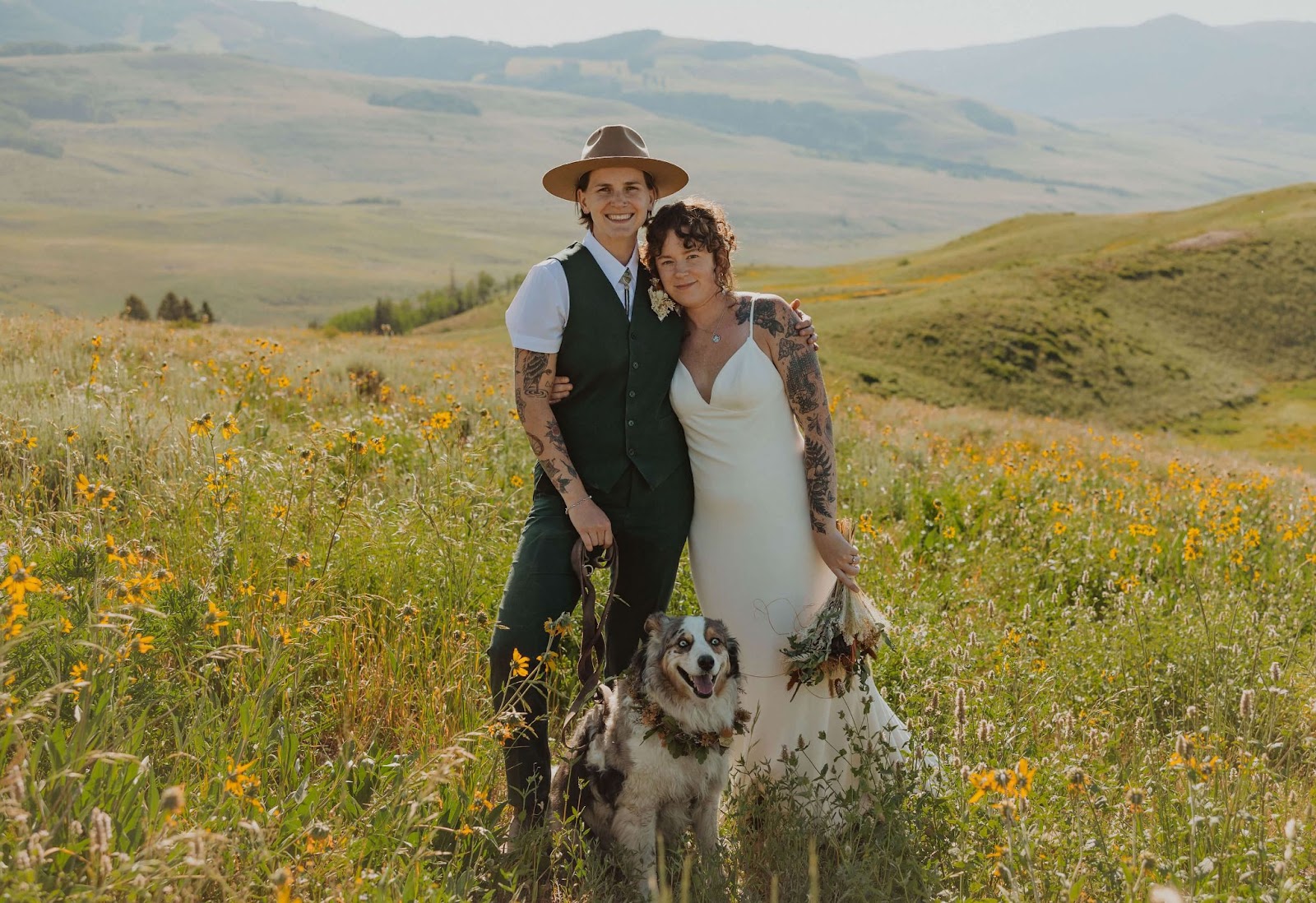 couple and dog posing for wedding picture in field of flowers