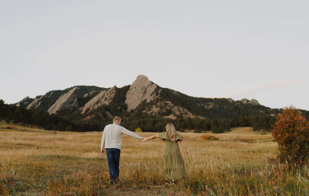 couple holding hands facing mountains while posing for engagement photos in Colorado