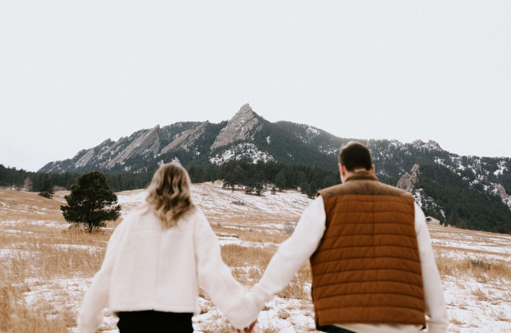 couple holding hands facing away from camera towards mountains for engagement photo session