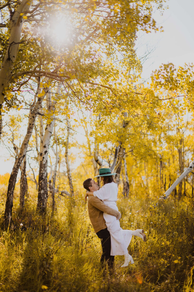 Couple hugging and smiling at each other while posing for engagement photos in Colorado surrounded by trees