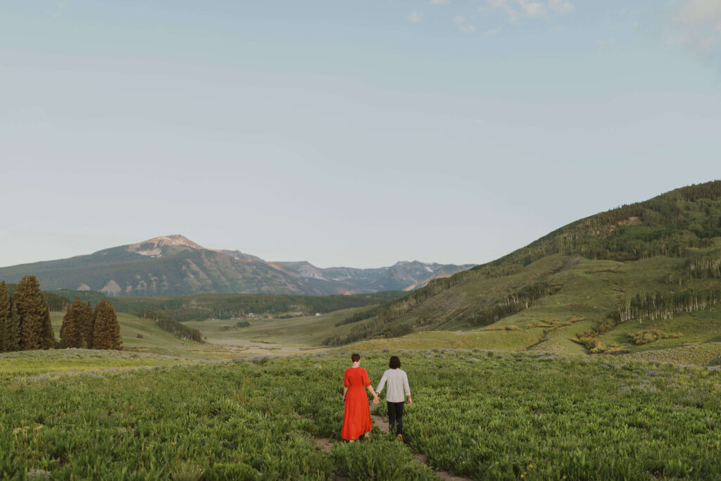 Couple holding hands walking away from camera towards mountains