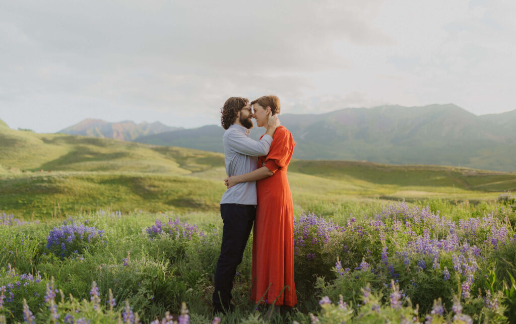 couple hugging and looking at each other surrounded by mountain scenery and wildflowers