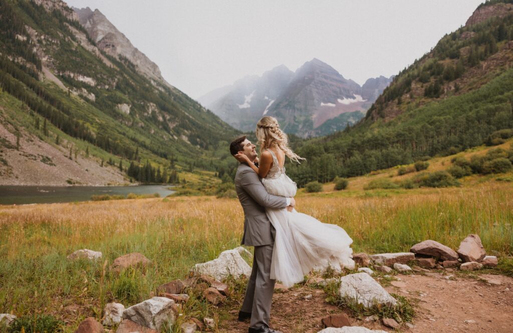 Groom holding bride and smiling backed by Maroon Bells mountain