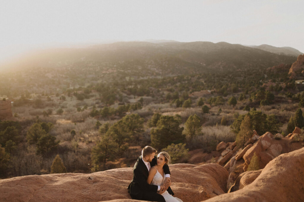 Bride and groom sitting on a red rock backed by mountains