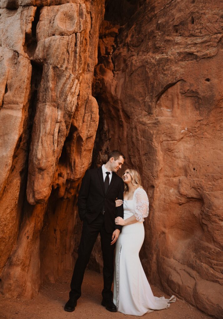 couple standing and looking at each other surrounded by red rocks at Garden of the Gods