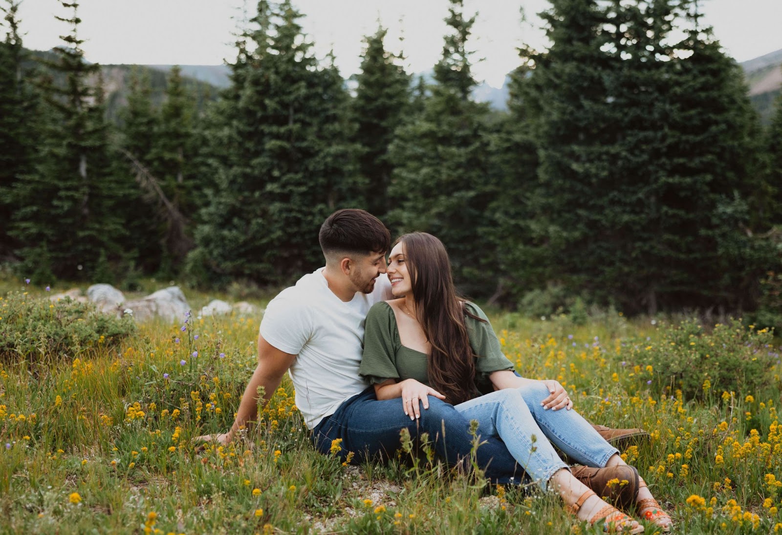 Couple sitting together in field of wildflowers surrounded by trees