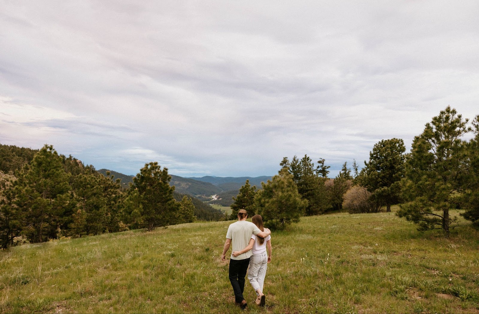 couple facing mountains and trees with arms around each other posing for engagement photos