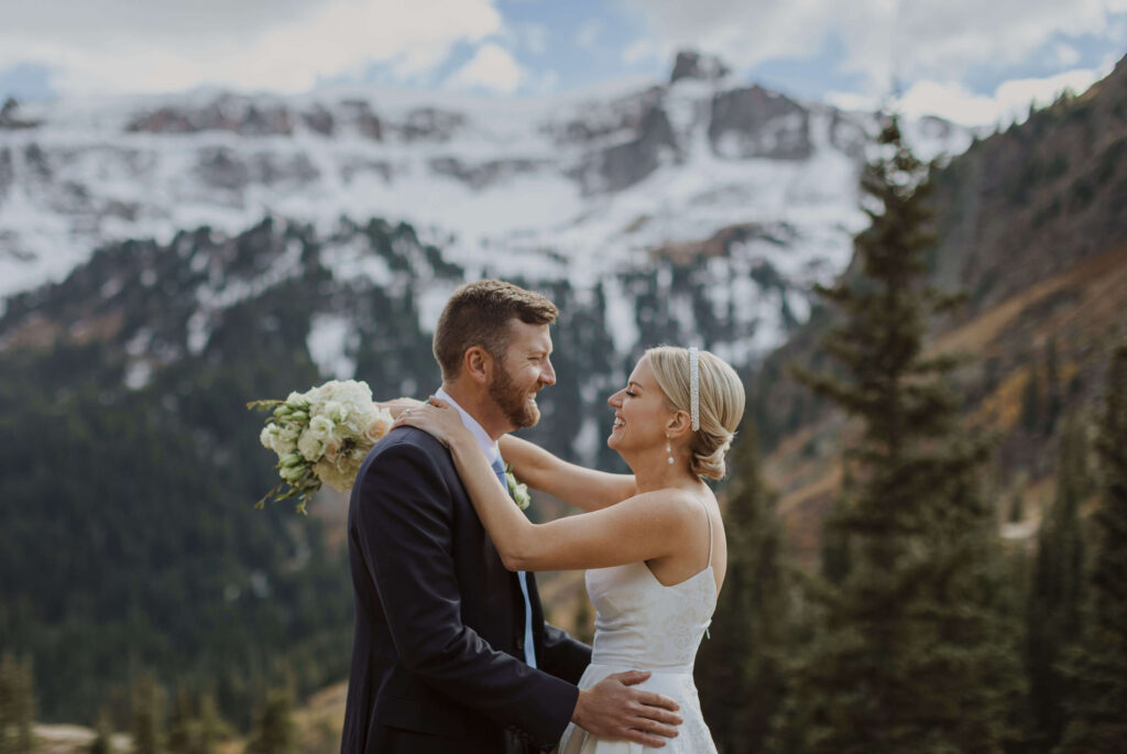 Bride and groom smiling at each other backed by San Juan Mountains