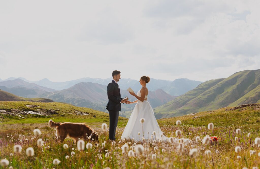 Bride reading vows to groom standing in a field surrounded by the San Juan Mountains