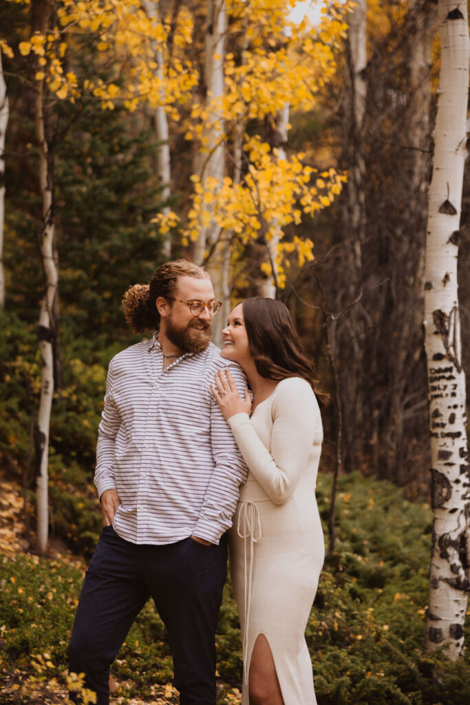 Couple posing for engagement photos surrounded by trees