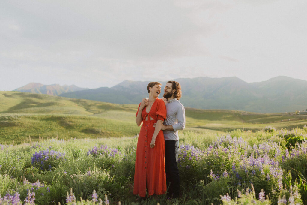 Couple posing for engagement photos in a field with wildflowers