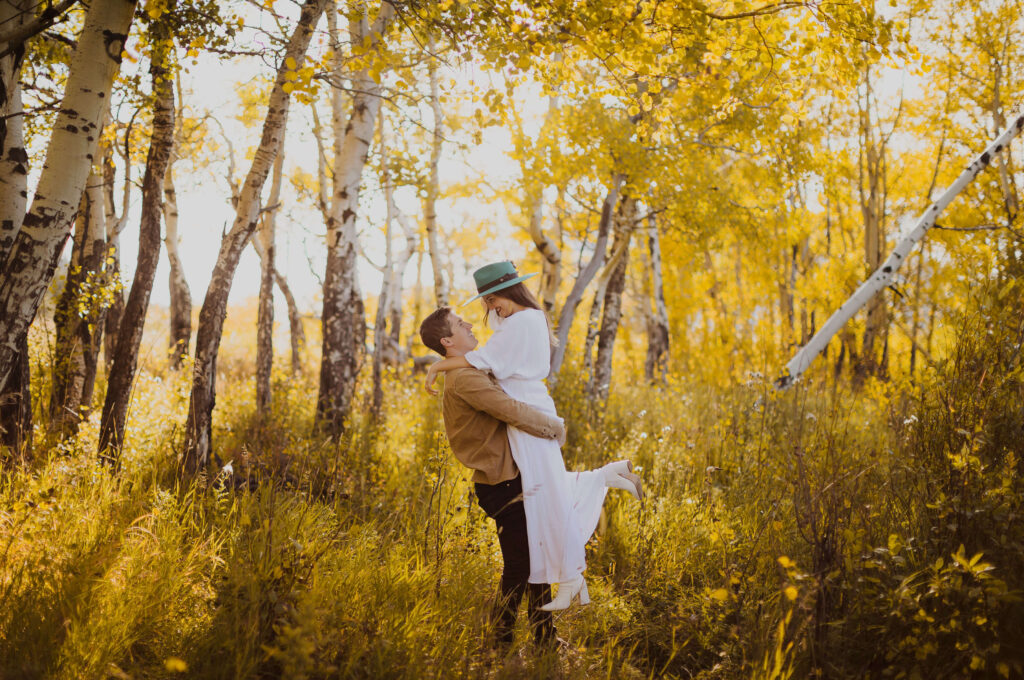 couple hugging and looking at each other surrounded by trees and fall foliage for engagement photos