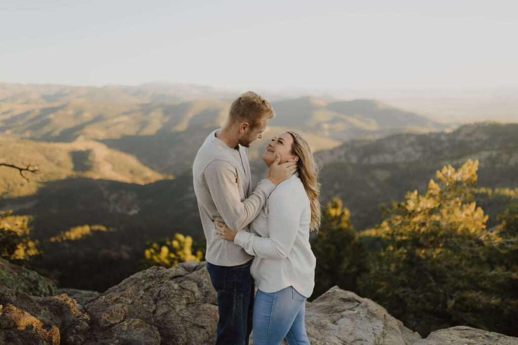 Couple looking at each other and smiling for engagement photos and surrounded by mountain scenery