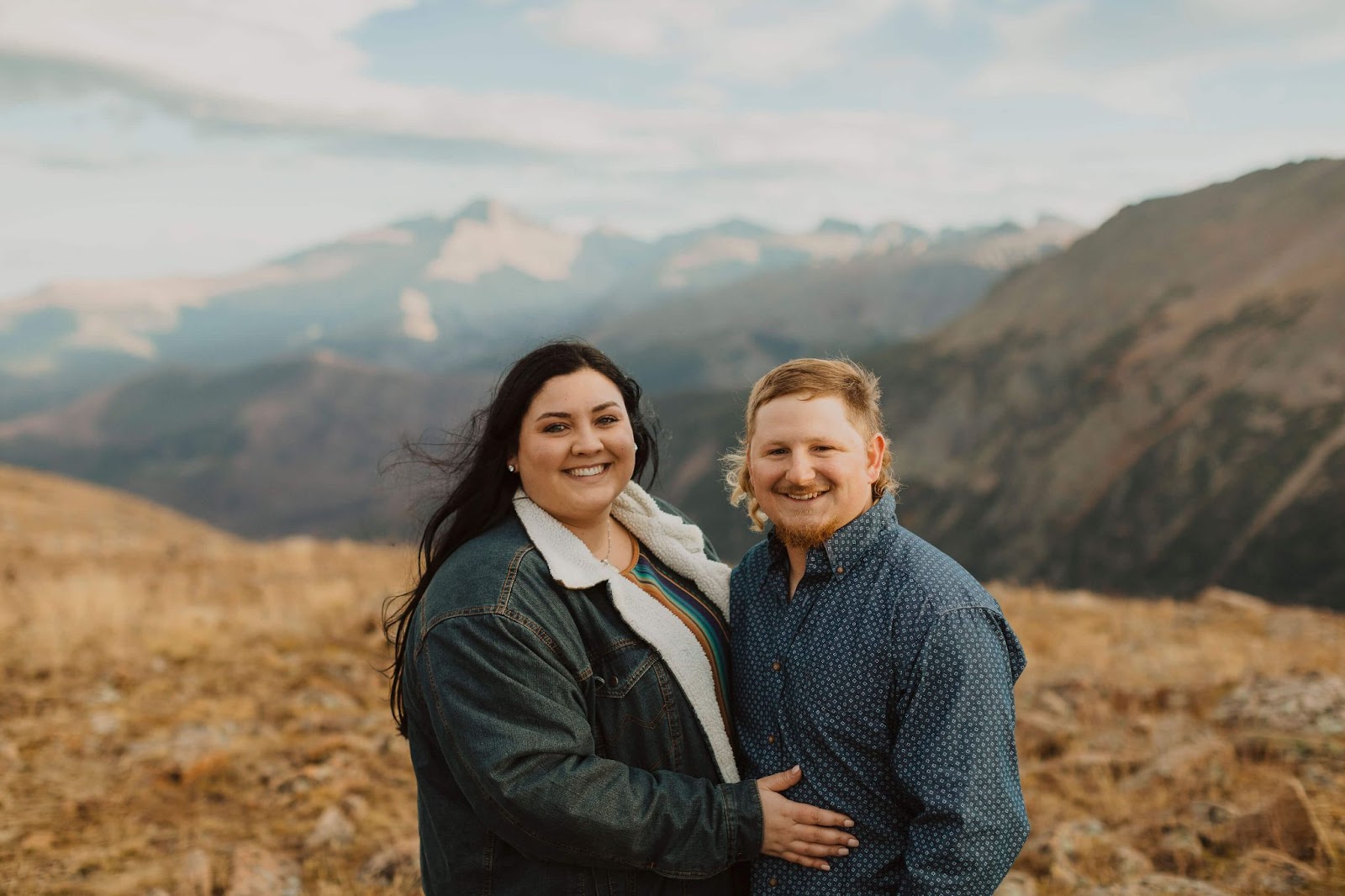 Couple smiling at camera backed by mountain scenery for Rocky Mountain National Park engagement photos