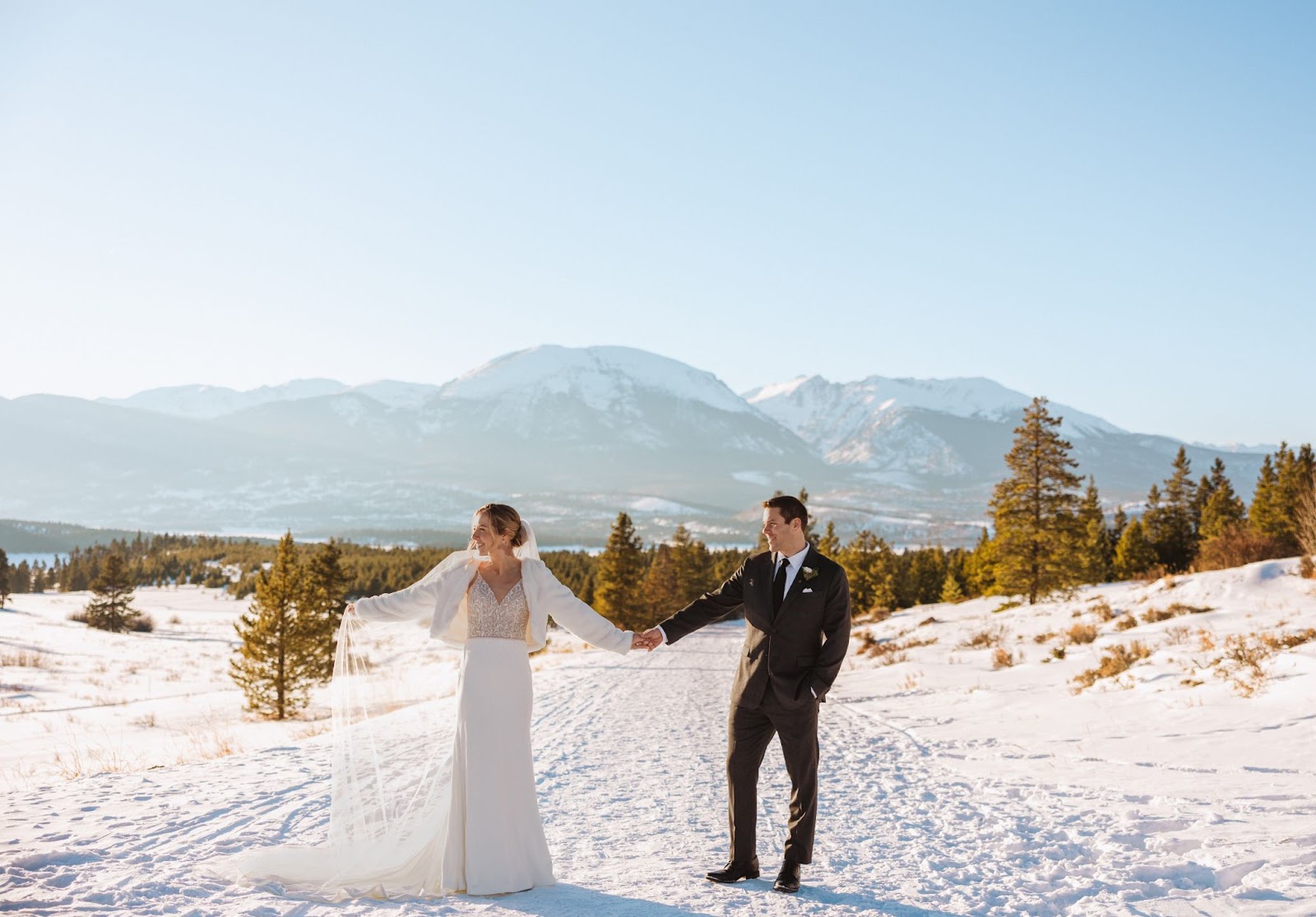 Bride and groom holding hands surrounded by snow and mountain scenery in Breckenridge