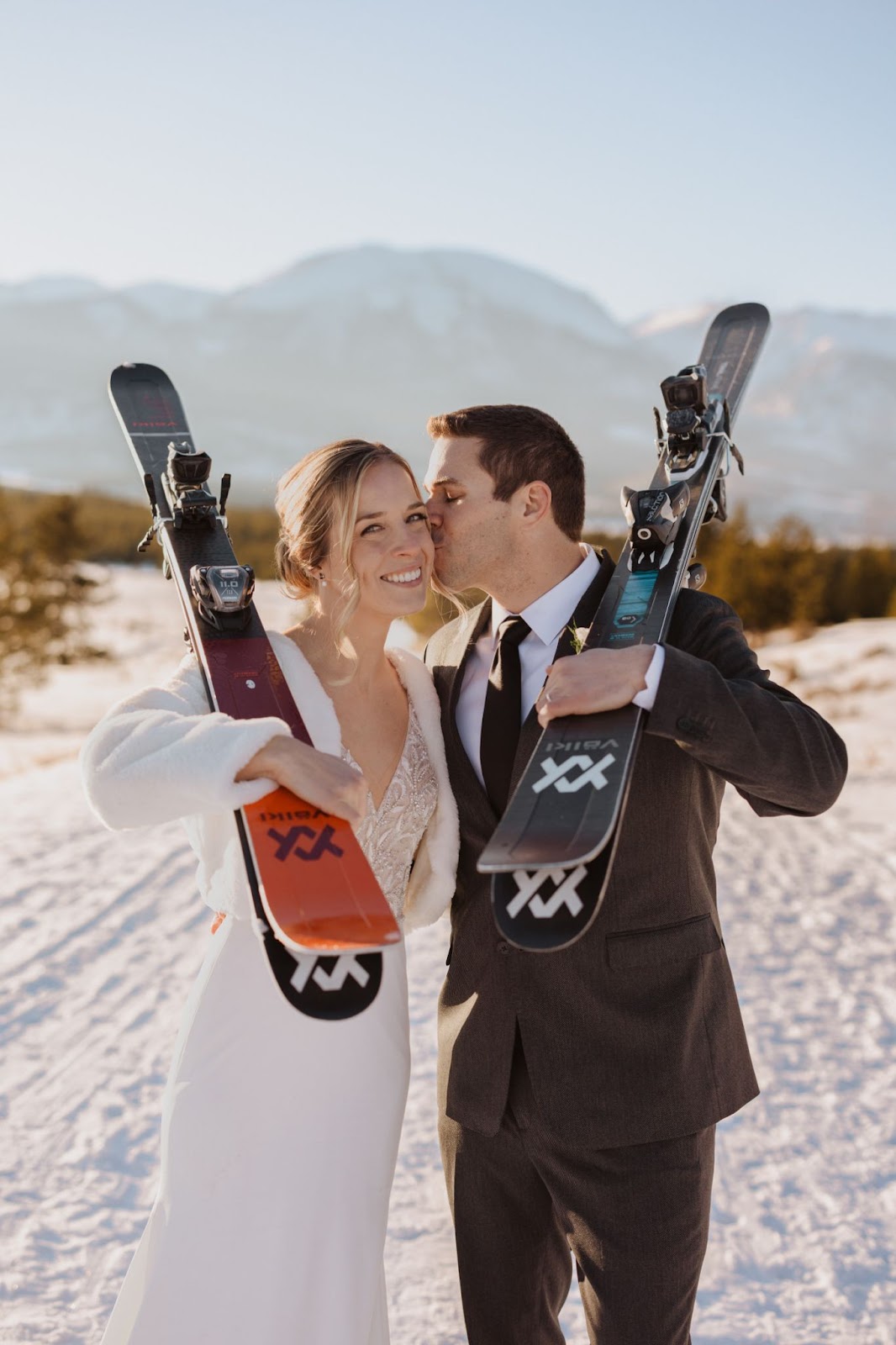 Bride and groom holding skis surrounded by snow and mountains