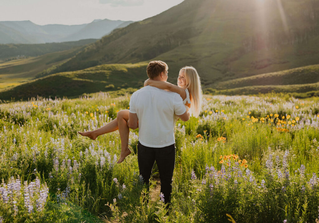Couple posing for proposal photos surrounded by wildflowers and mountains