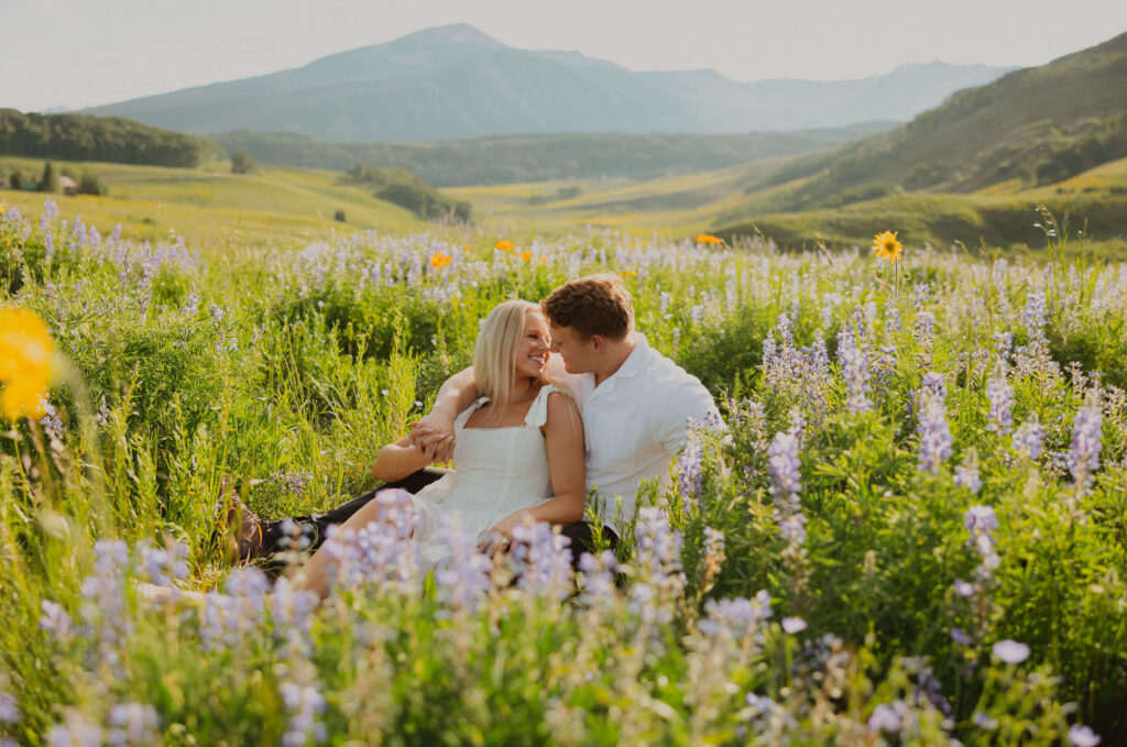 Couple sitting surrounded by wildflowers for proposal photos in Colorado