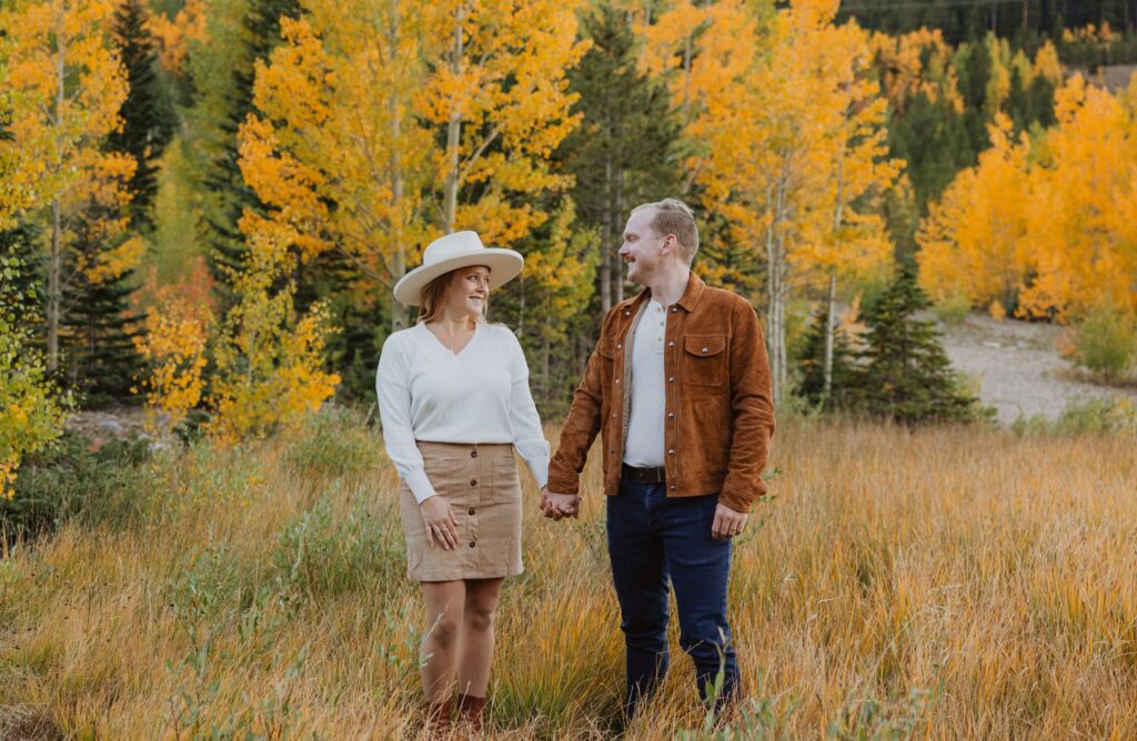 Couple holding hands and smiling surrounded by fall foliage
