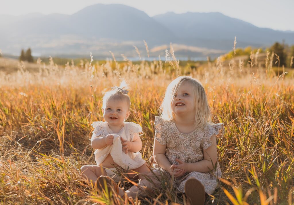 sisters sitting in grass backed by mountain scenery near Denver