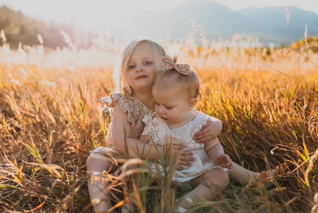 sisters sitting in grass backed by mountain scenery near Denver