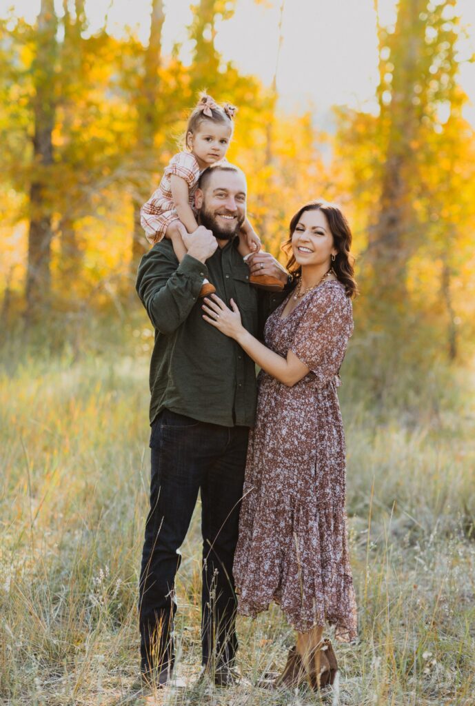 Mom, dad, and daughter posing for family photos in Denver surrounded by trees