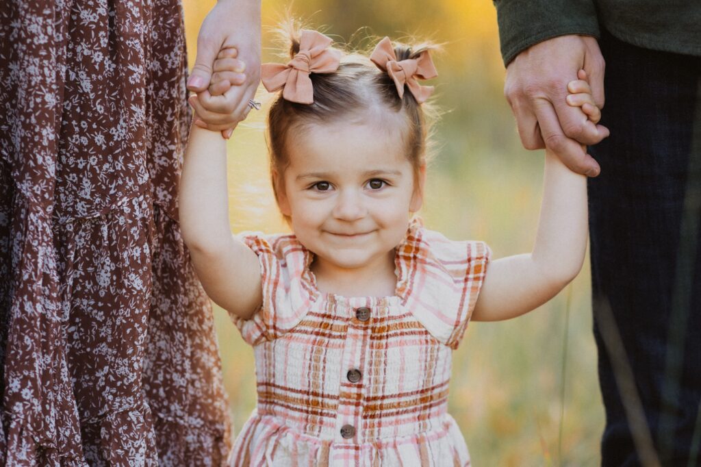 child smiling at camera holding parents hands