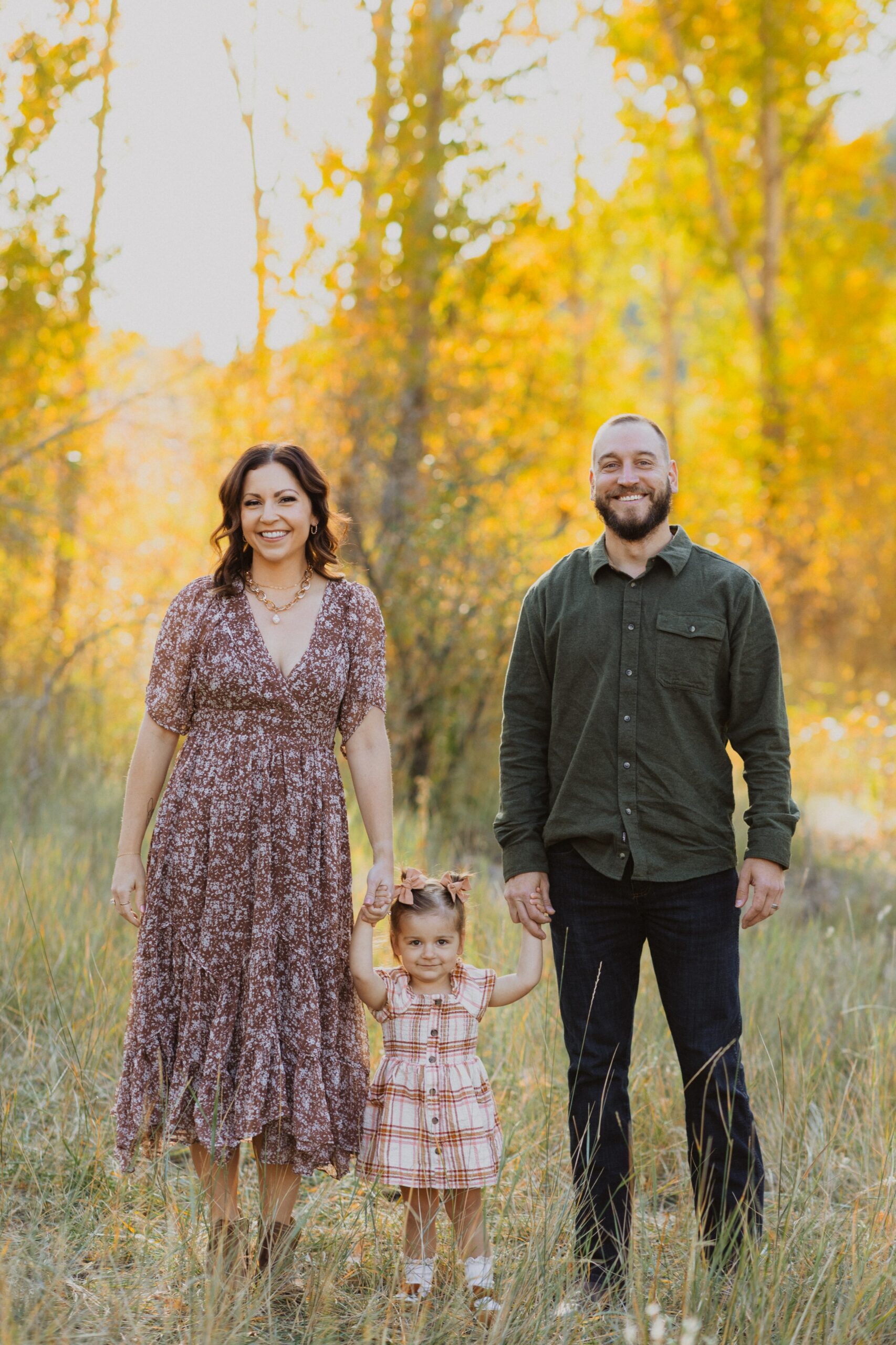 mom, dad, and daughter posing for family photos in Denver surrounded by trees