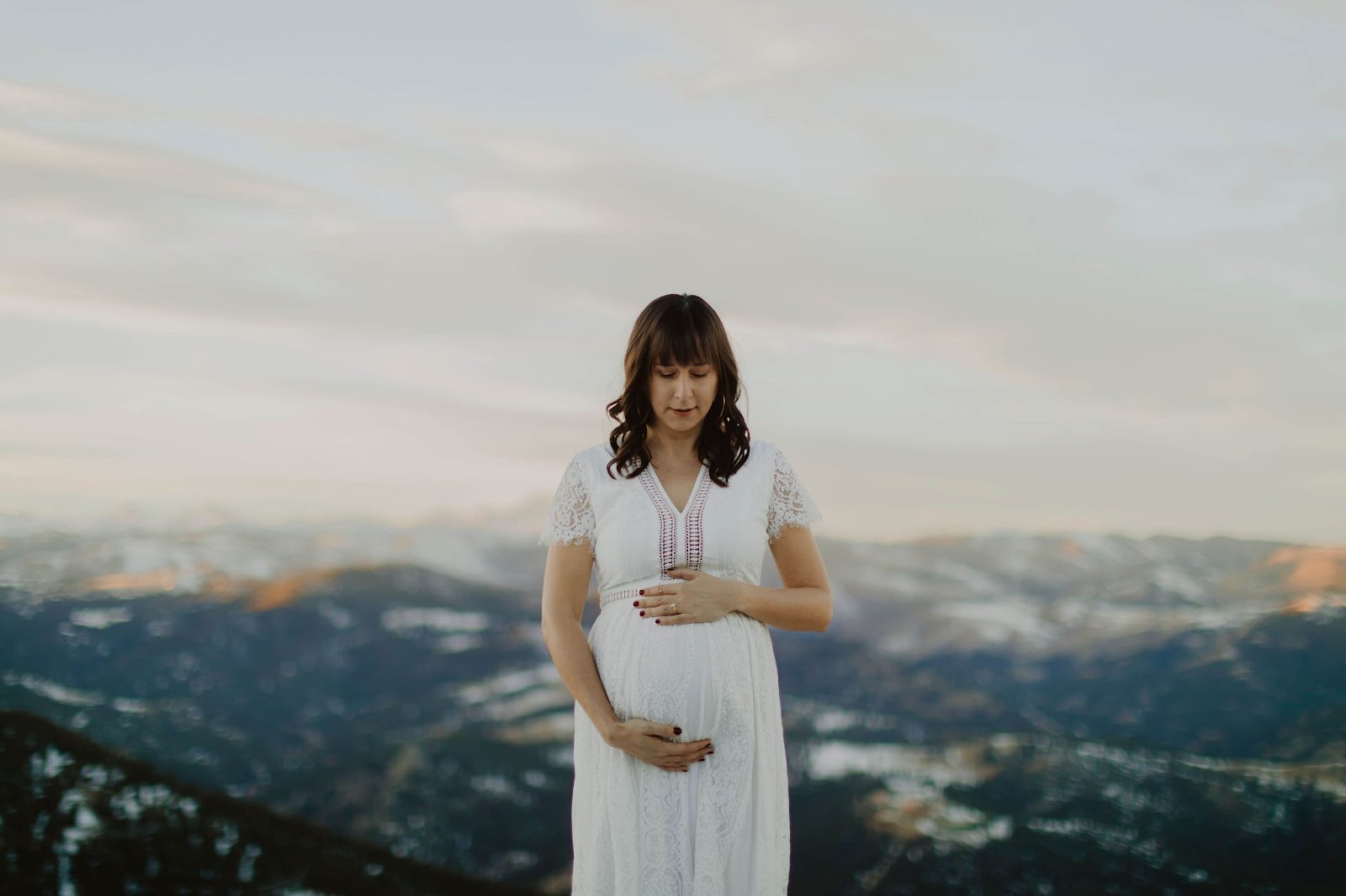 Woman in white dress looking down at baby bump