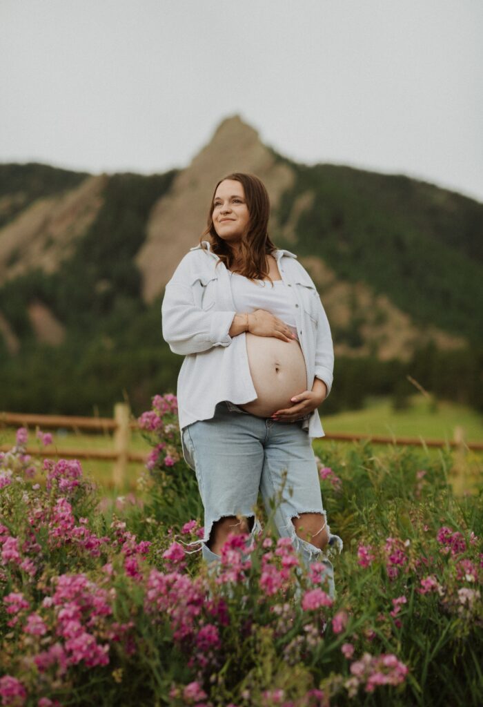 Woman surrounded by pink flowers showing baby bump for maternity photos