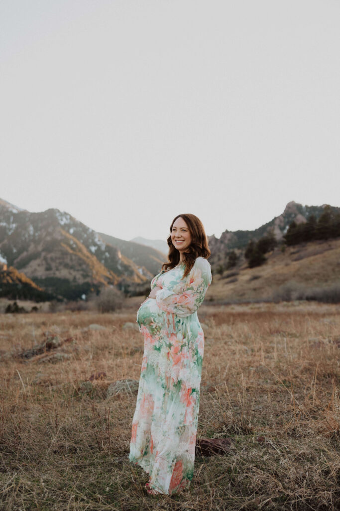 Woman in long floral dress smiling while holding baby bump