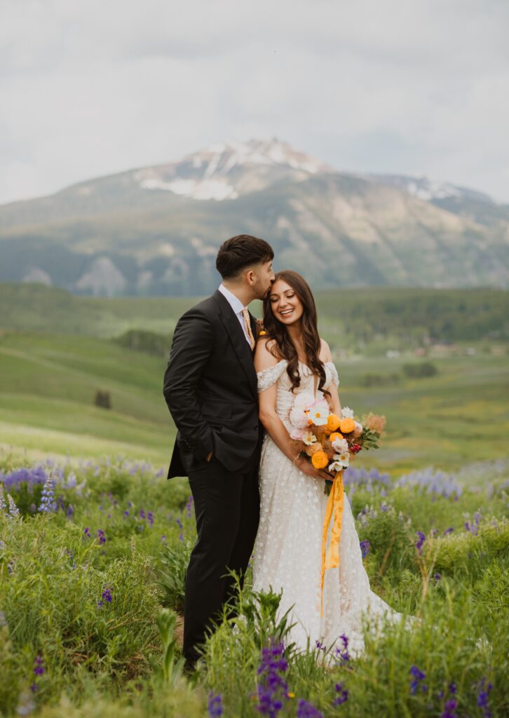 Bride and groom posing for wedding photo surrounded by mountain scenery and purple flowers