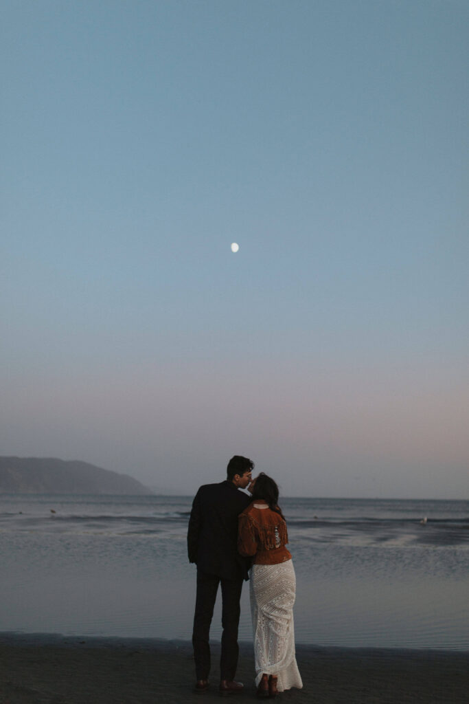 bride and groom kissing and facing the ocean