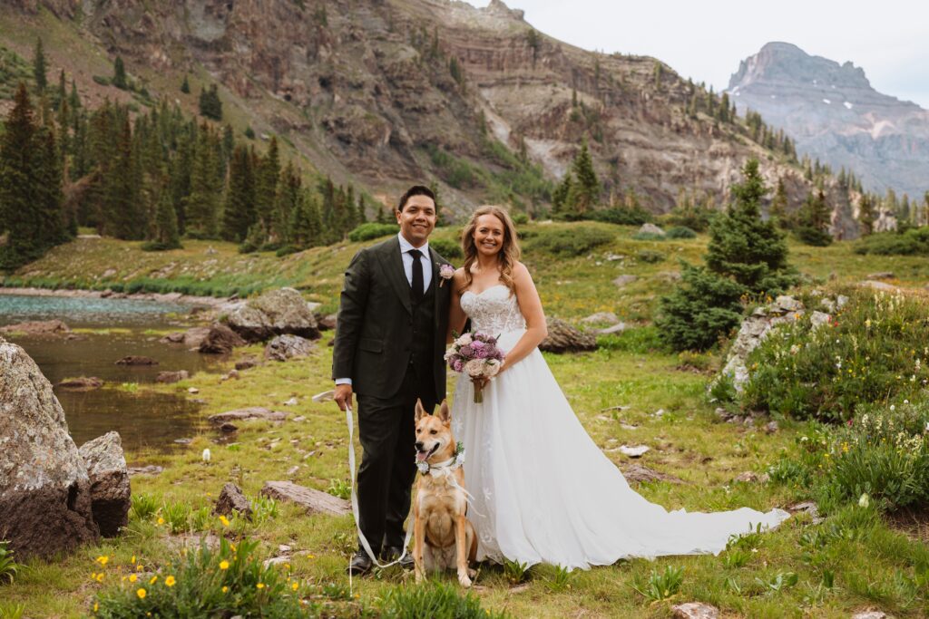 bride, groom, and dog posing for wedding photos surrounded by mountains in Ouray
