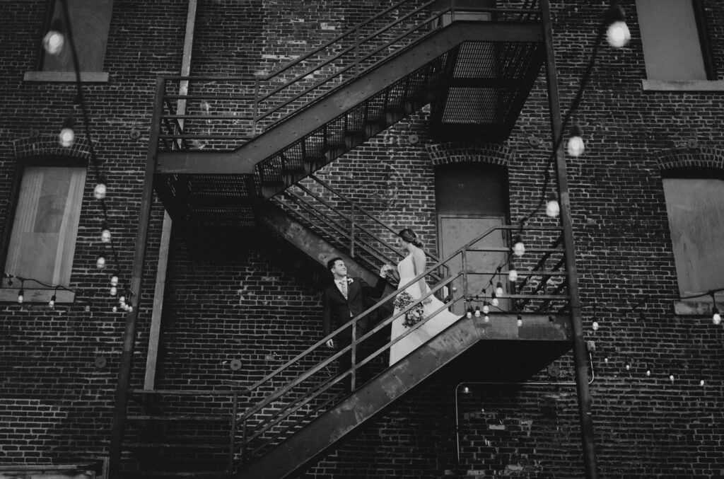 Bride and groom walking down stairs beside brick building for Kansas City wedding