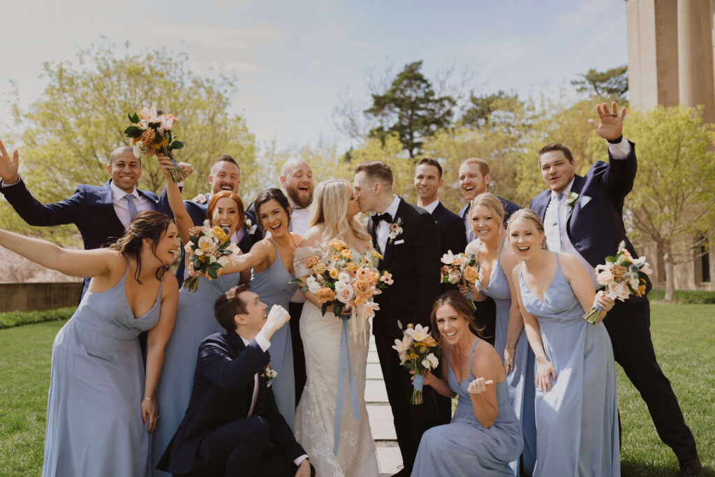 Wedding party standing around bride and groom kissing for Kansas City wedding