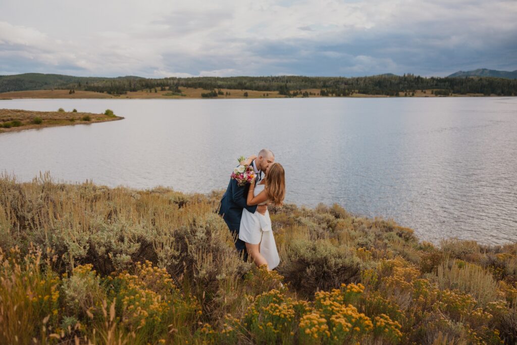 Bride and groom hugging and kissing by lake at Bella Vista Estate in Steamboat Springs