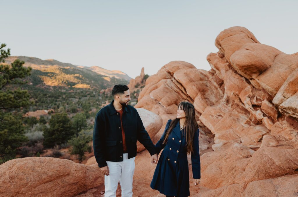 Couple smiling at each other at standing in front of red rock formation for engagement photos in Colorado Springs